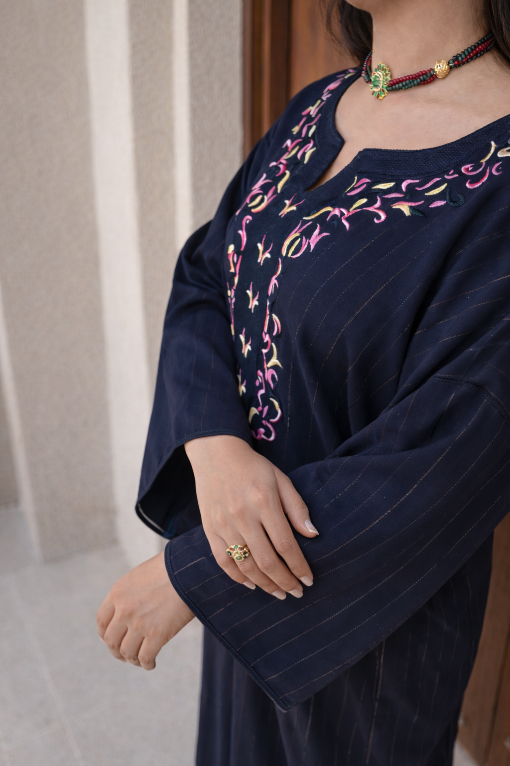 Detailed view of the intricate gold thread-work on the butterfly sleeves of the dark magenta kaftan.