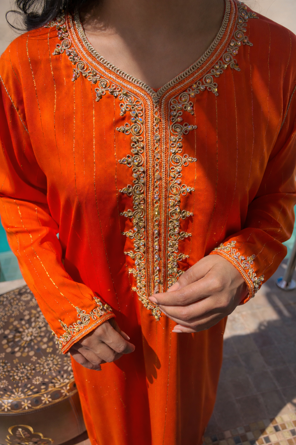 Detailed view of the intricate gold thread-work on the flowing sleeves of the sunset orange kaftan.