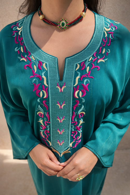 Close-up of the magenta, ivory, and gold floral embroidery on the emerald-teal matte fabric.