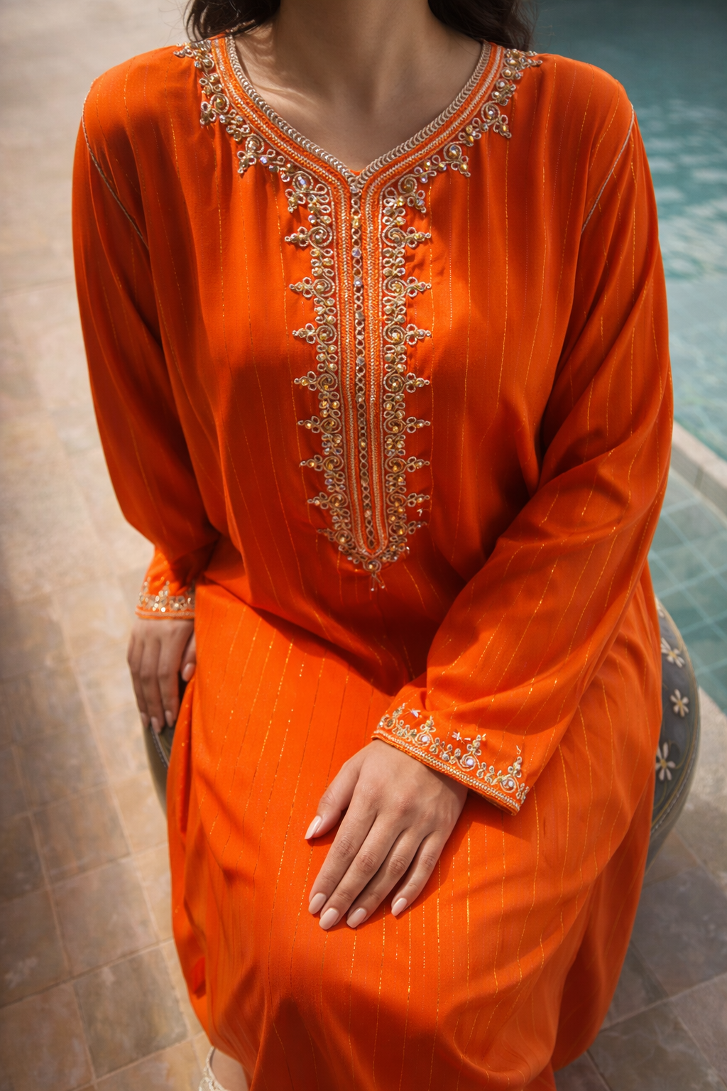 Close-up of the ornate gold embroidery and shimmering crystals on the V-neckline of the orange Maison Nelya kaftan.