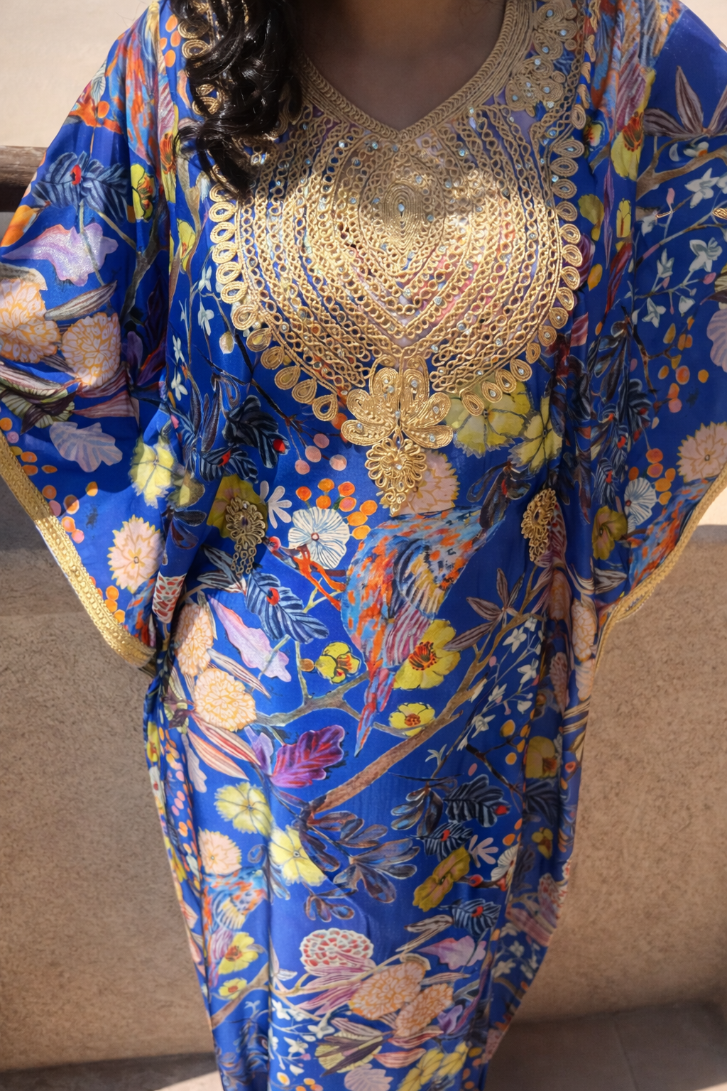 Full view of the Maison Nelya Sapphire Blossom Kaftan featuring a blue floral patterned fabric with gold embroidery.