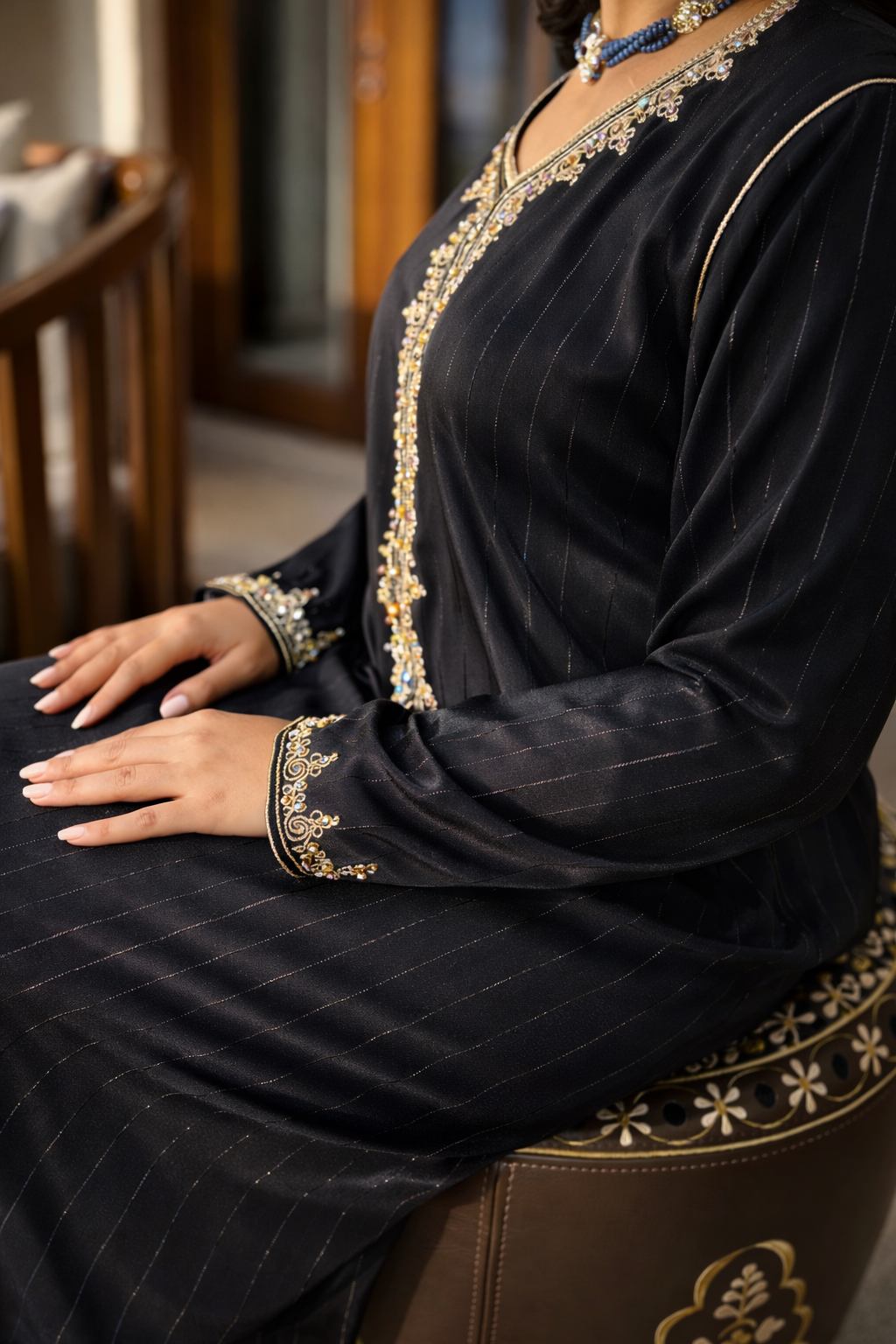 Detailed view of the gold-embroidered cuffs and the subtle metallic pinstripe texture of the Maison Nelya black abaya.